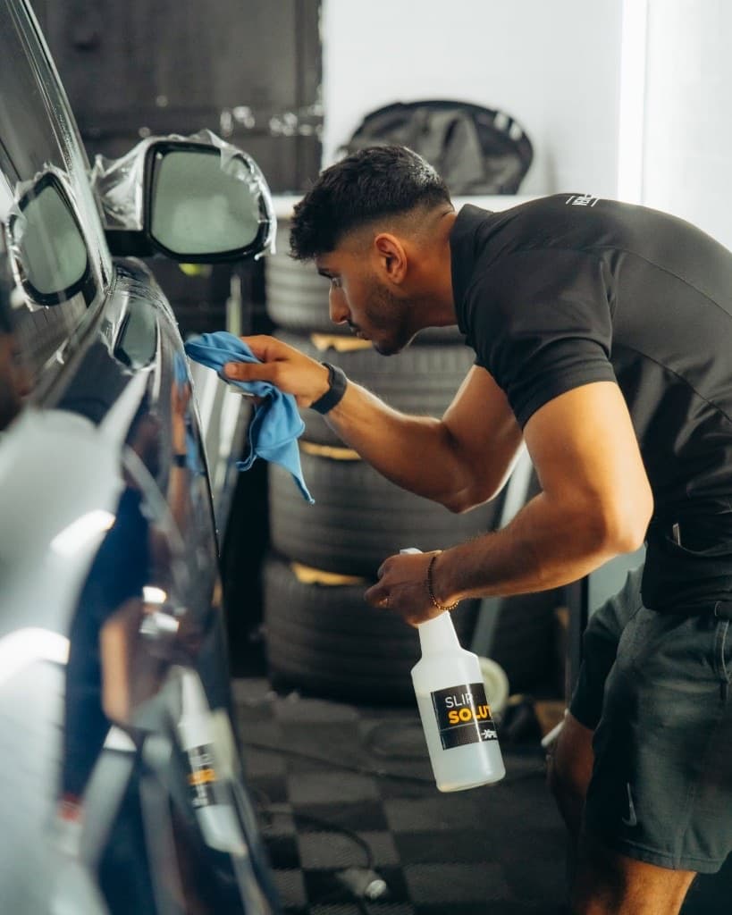 JnJ detailer hand-finishing the flank of a dark vehicle in the climate-controlled studio