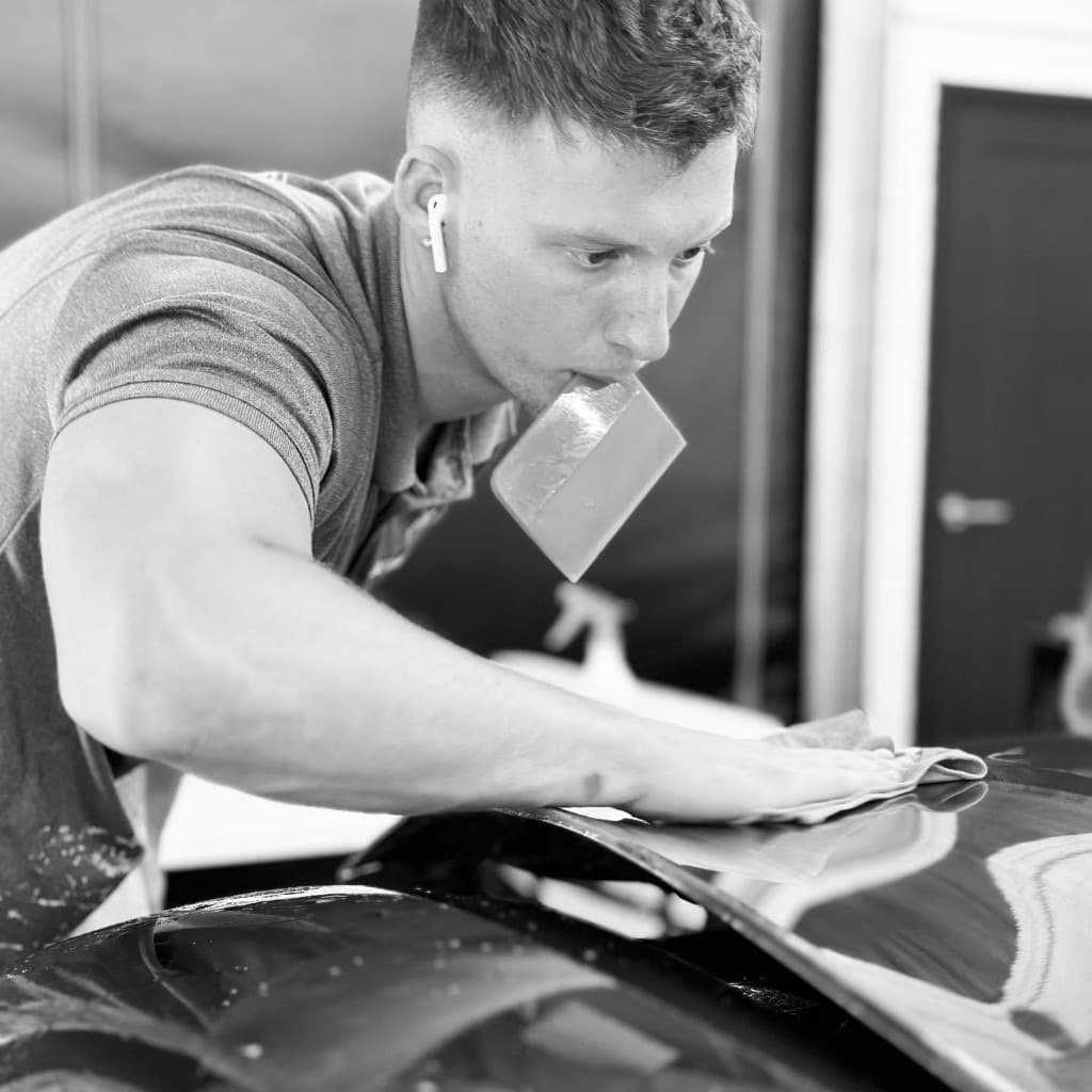 JnJ technician refining a black bonnet by hand during multi-stage paint correction