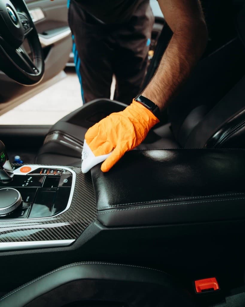 Gloved JnJ detailer deep-cleaning the leather and carbon trim inside a BMW interior