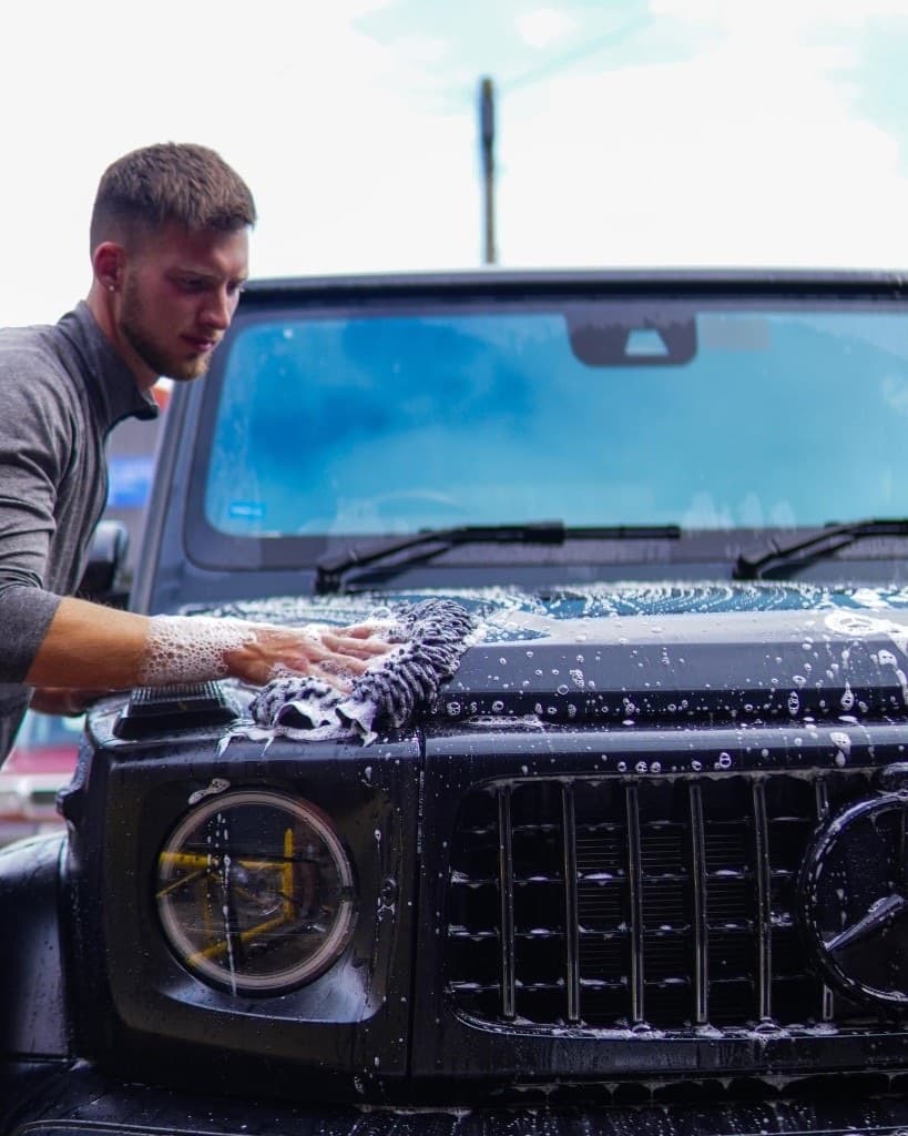 JnJ detailer foam-washing the front of a black Mercedes G-Wagon during a mobile valet